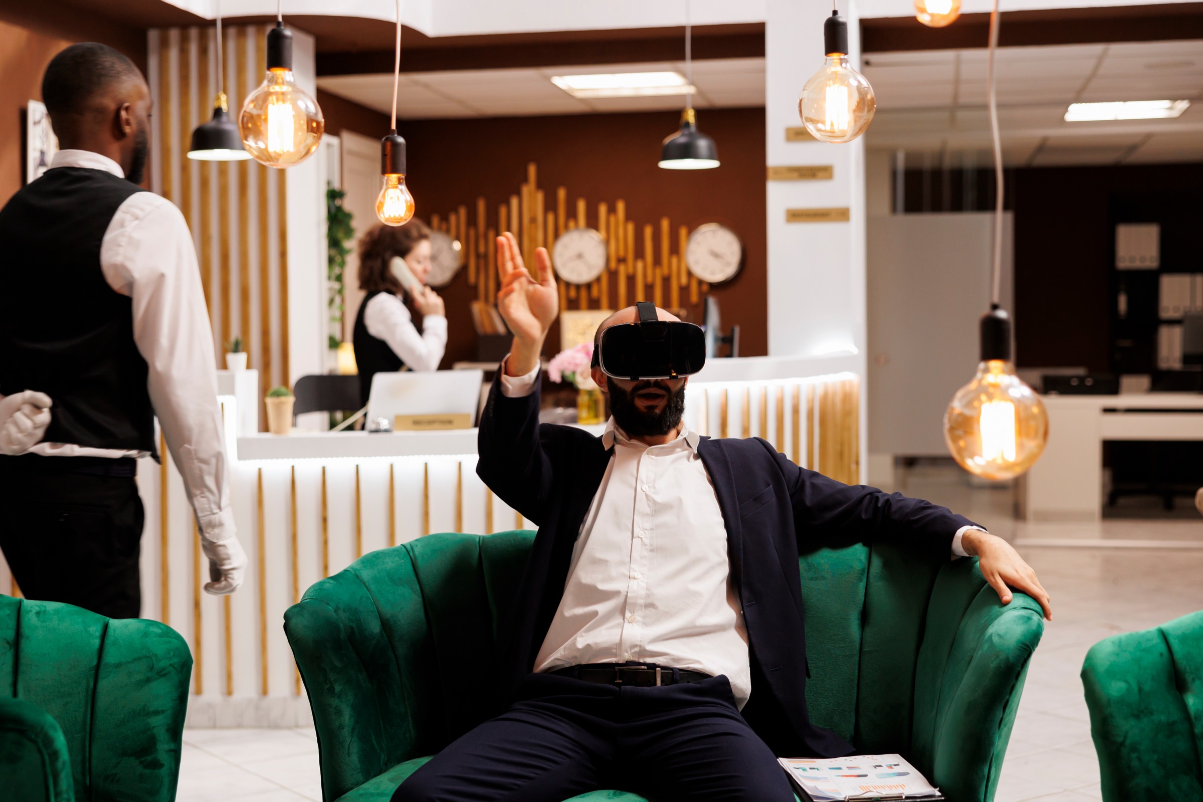 A guest relaxing in a hotel lobby while staff work at reception